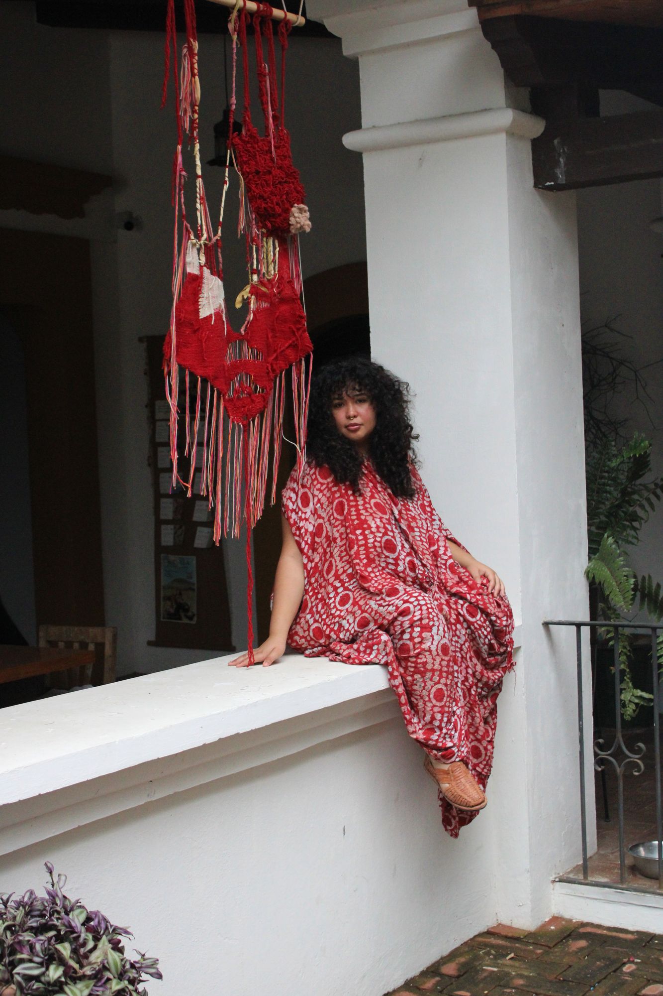 Natalia Hernandez seated on a white ledge in a courtyard, wearing a red patterned dress