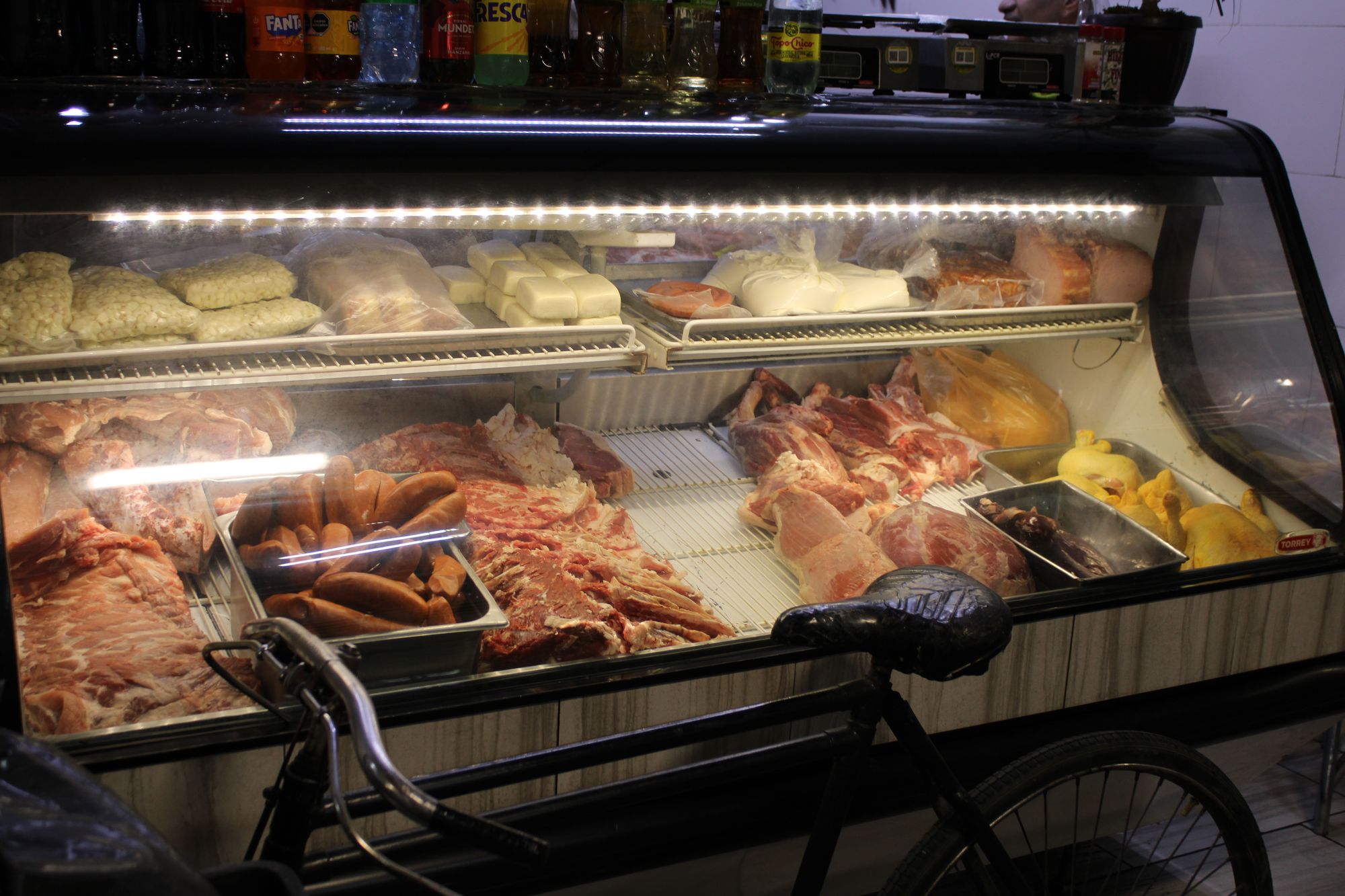 Lit meat and cheese display case with a repaired bike seat in front